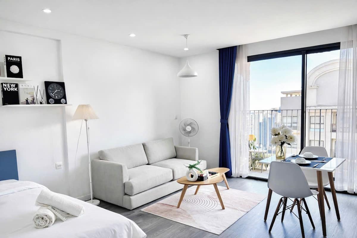Une chambre d’hôtel moderne équipée d’un canapé, d’une table à manger avec des chaises, d’un ventilateur et d’une grande fenêtre avec des rideaux.