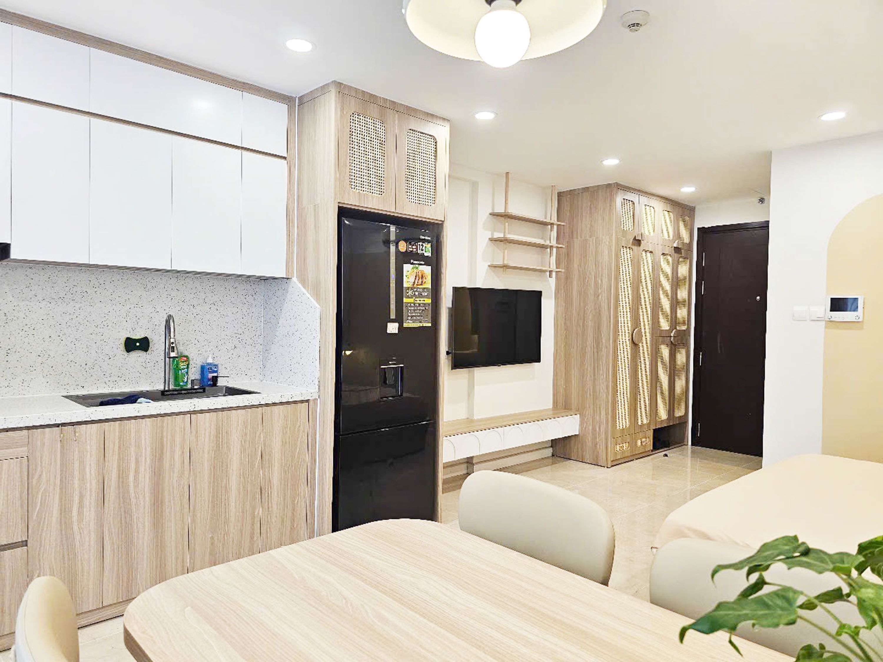 A modern kitchen with a built-in refrigerator, a flat-screen TV, and a dining area with a table and chairs.