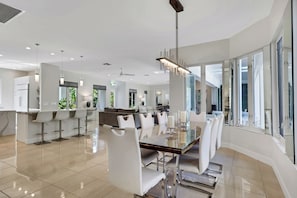 A modern dining area with a glass table, white chairs, and a ceiling fan. - EverHouse at the Moorings (Naples)
