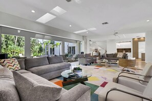 Un salon moderne comprenant un canapé, des fauteuils, une table basse et offrant une vue sur un jardin tropical grâce à de grandes fenêtres.