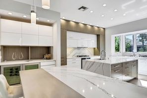 A modern kitchen with white cabinetry, a marble island, and a built-in oven. - EverHouse at the Moorings (Naples)
