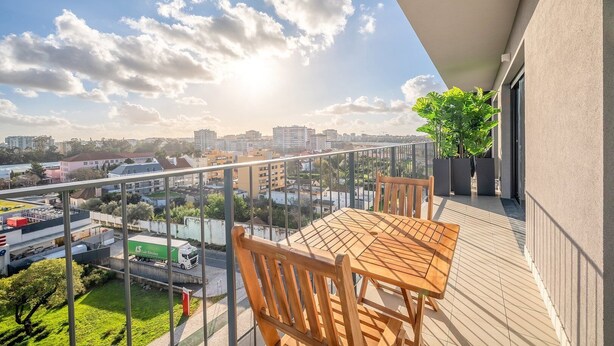 Un balcon avec une table et des chaises en bois, donnant sur un paysage urbain composé d’immeubles et d’une route.