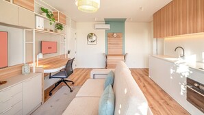 Une cuisine moderne dotée d’un four encastré, un coin repas avec une table et des chaises en bois, et un espace salon confortable avec un canapé et des coussins.
