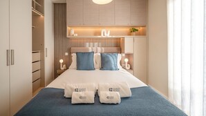 Une chambre d’hôtel moderne équipée d’un lit, de tables de chevet, d’une armoire et d’un luminaire suspendu.