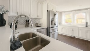 Uma cozinha moderna com armários brancos, eletrodomésticos de aço inoxidável e uma grande janela que permite entrada de luz natural.