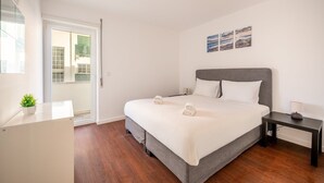 Ein modernes Hotelzimmer mit einem großen Bett, einem Nachttisch, einer kleinen Nachttischlampe und Blick durch eine Glastür.