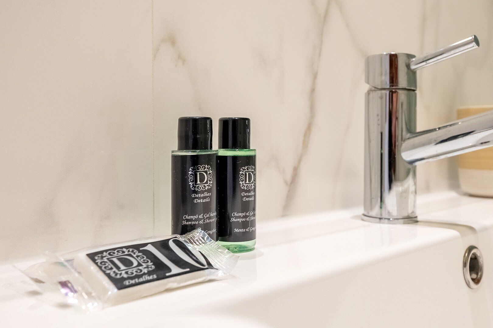 Een badkamer met een marmeren wand, een chromen kraan en twee flessen shampoo en conditioner.