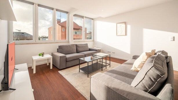 Ein modernes Wohnzimmer mit einem grauen Sofa, einem Glastisch und einem weißen Beistelltisch.