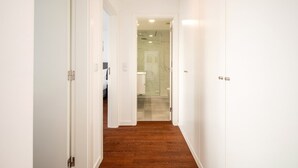 Ein Korridor mit weißen Wänden, Holzboden und einer Glastür zu einem Badezimmer.
