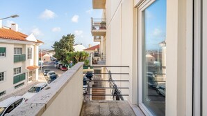 Ein Balkon mit Blick auf eine Straße, geparkte Autos und ein Gebäude mit Ziegeldach.