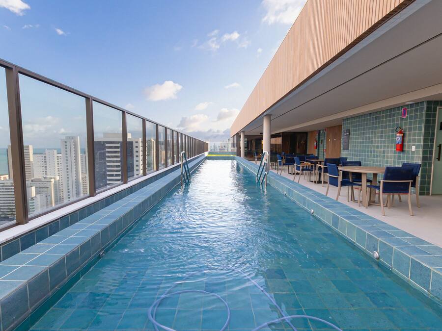 A rooftop infinity pool with a city view, a seating area with tables and chairs, and a tiled floor.