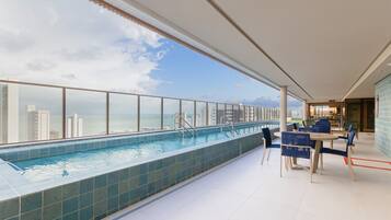 Piscina no terraço com vista para o horizonte da cidade e área de refeições com mesas e cadeiras.