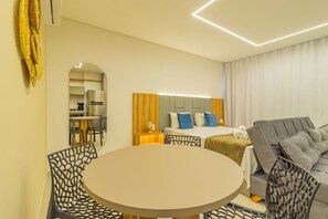 A modern hotel room with a round dining table, a sofa, a bed with blue and white bedding, and a wooden headboard. - Icon Housi in Boa Viagem New 300m From the Sea By Carpediem (Recife)