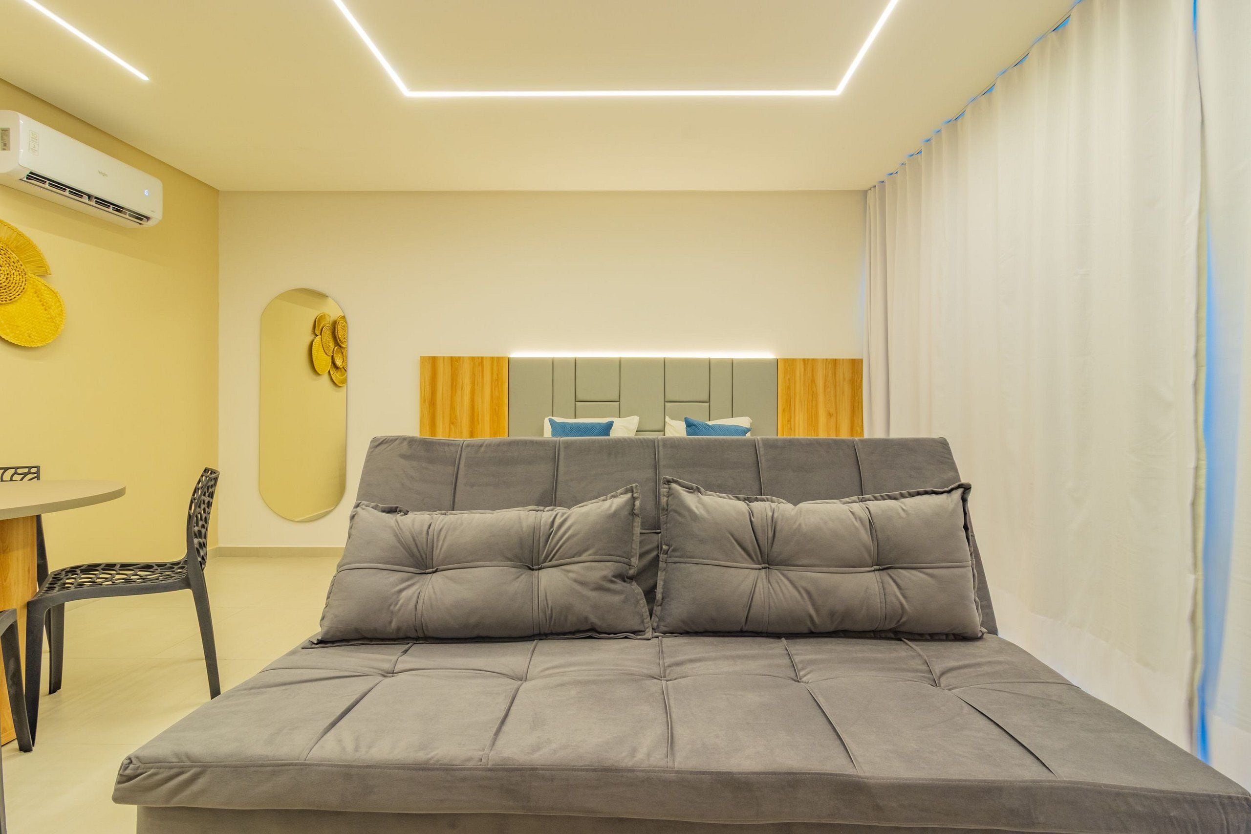Un dormitorio moderno con un sofá cama gris, una mesita con una silla y un aire acondicionado instalado en la pared.