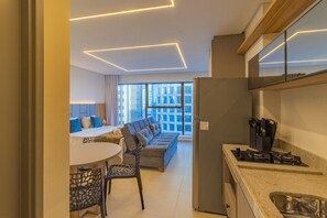 Eine moderne Küche mit Einbauherd, ein Essbereich mit rundem Tisch und Stühlen, und ein Sofa mit Blick auf die Stadt durch große Fenster.