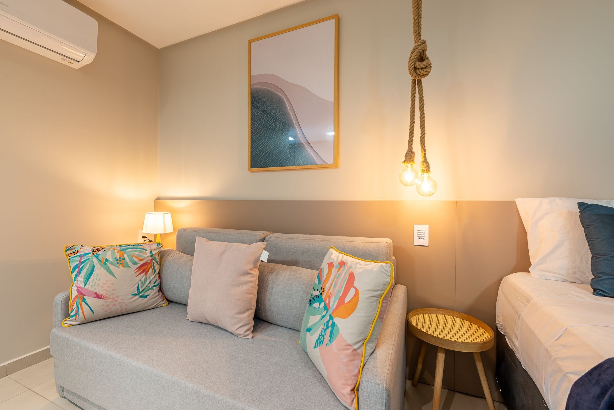 A room with a sofa, a bed, a wall-mounted light fixture, and a painting.