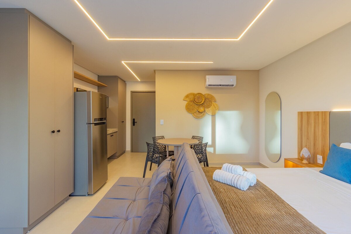 Een moderne hotelkamer met een bank, een bed, een eettafel met stoelen, een spiegel en een airconditioner aan de muur.