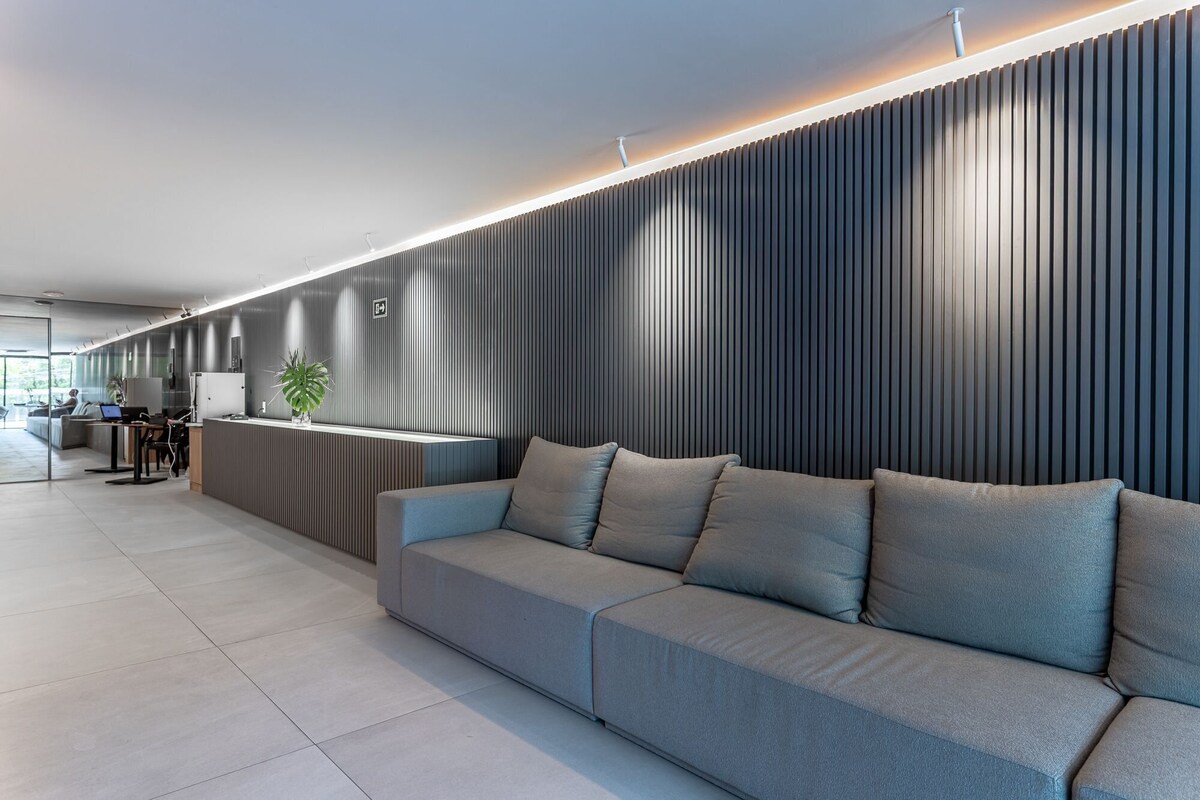 Un espace d’accueil moderne avec un canapé gris, un comptoir d’accueil et un mur décoratif vertical.