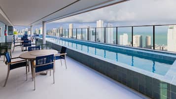Zona de piscina en la azotea con vistas a la ciudad, mesas y sillas.