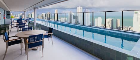 A rooftop pool area with a city view, tables, and chairs.