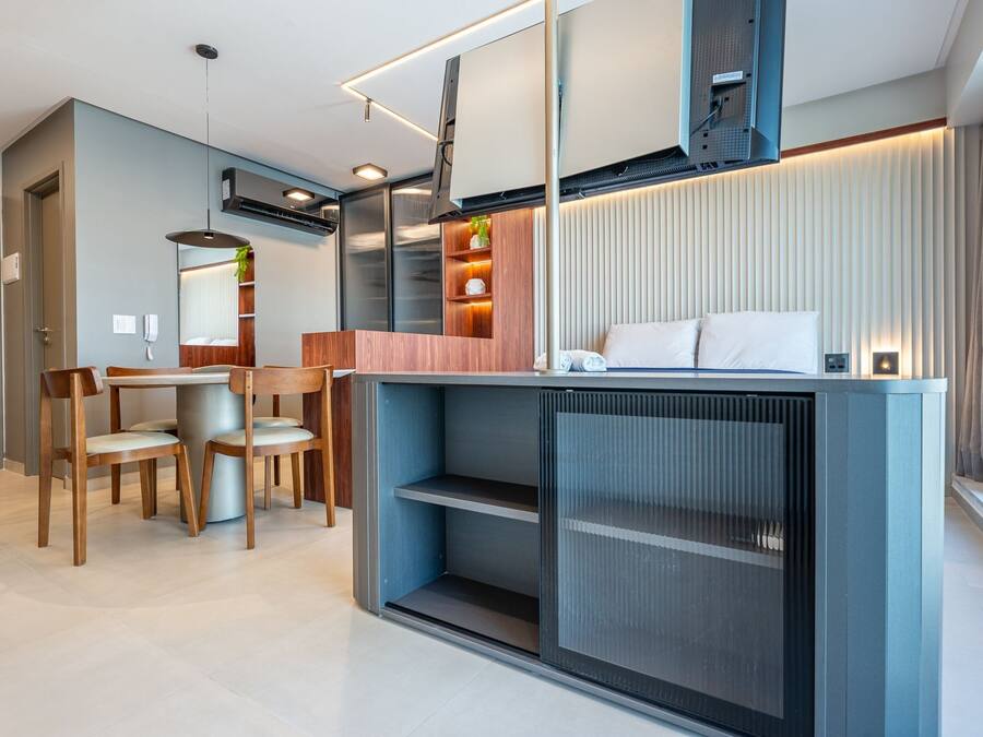 A modern hotel room with a dining area, a bed with a headboard, and built-in storage.