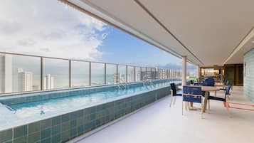 Una piscina en la azotea con vistas al horizonte de la ciudad y un área de comedor con mesas y sillas.