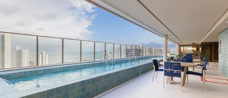 A rooftop pool with a view of the city skyline and a dining area with tables and chairs.