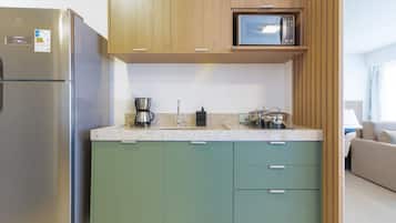 Una cocina compacta con un refrigerador de acero inoxidable, un microondas y un lavabo con hervidor.