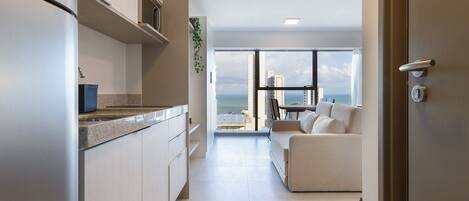 A modern kitchen with a view of the sea, a living area with a sofa, and a door with a key lock.