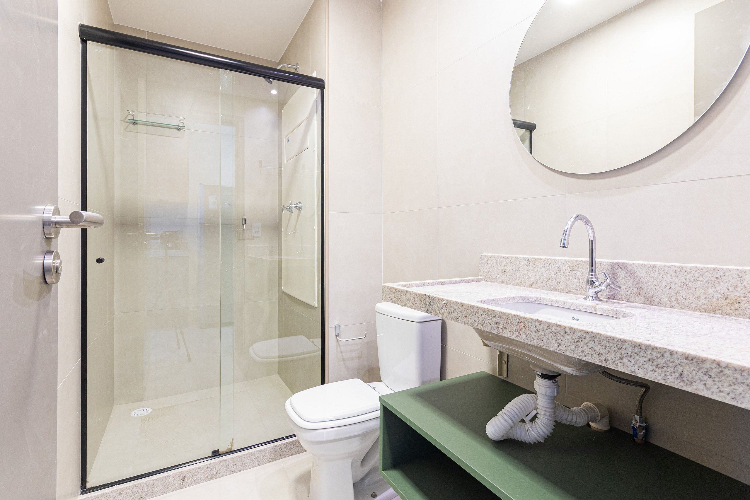 Une salle de bain moderne avec une douche à parois de verre, des toilettes blanches, un lavabo sur un plan de travail en granit et un meuble-lavabo vert.