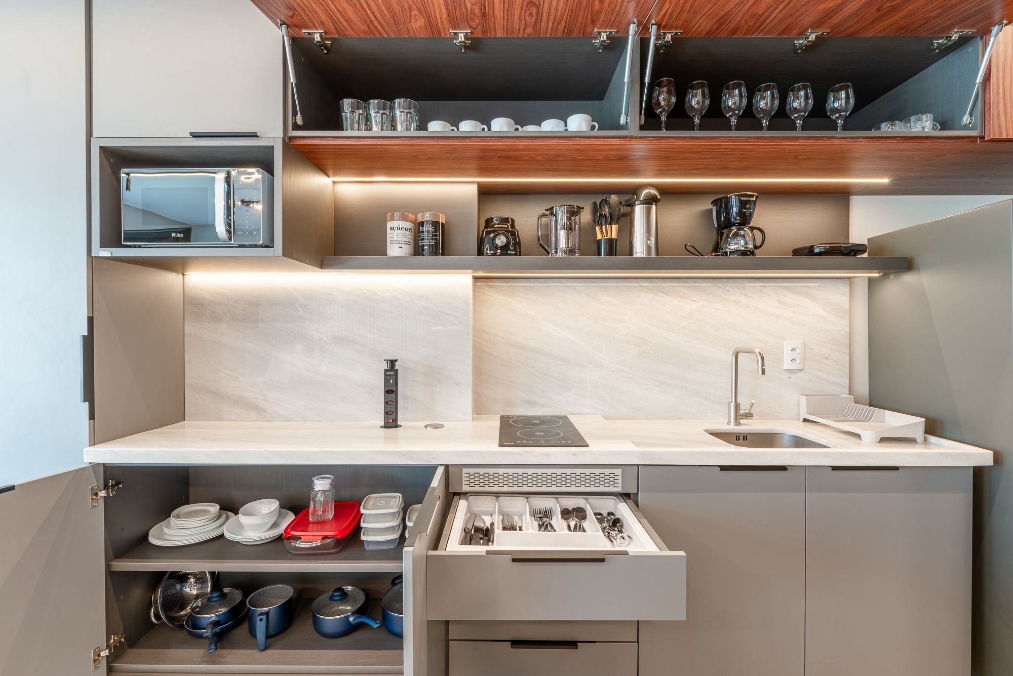 Una kitchenette compacta con cafetera integrada, microondas y un cajón con utensilios.