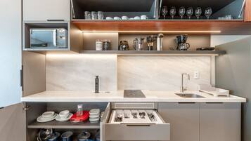 Una kitchenette compacta con cafetera integrada, microondas y un cajón con utensilios.