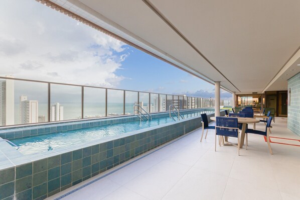 A rooftop pool with a view of the city skyline and a dining area with tables and chairs.