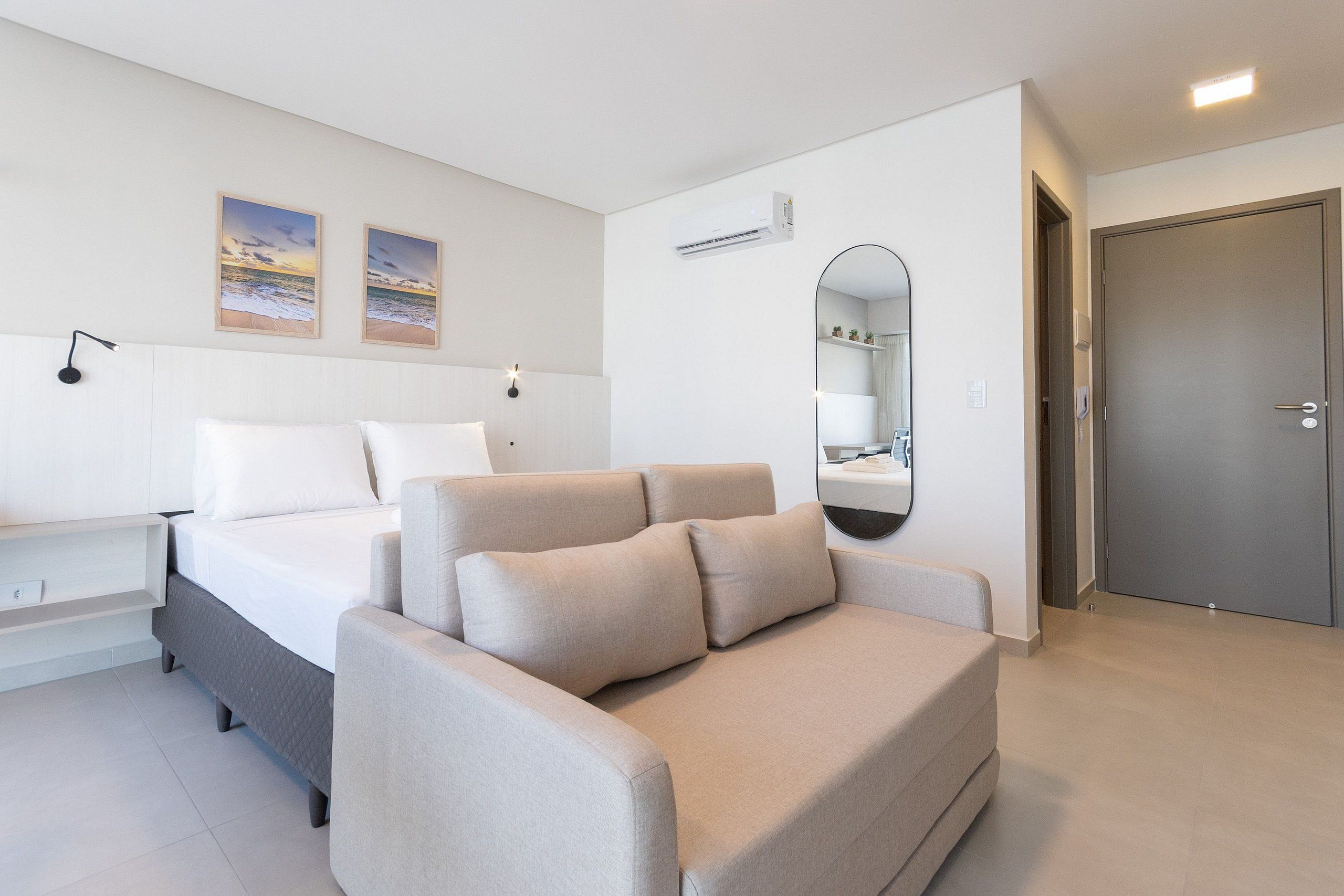 A modern bedroom with a bed, a sofa, a bedside table, a mirror, and a door.