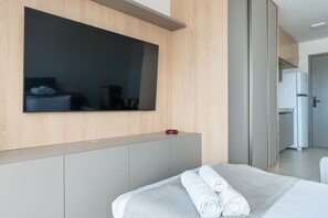 Ein modernes Hotelzimmer mit einem großen Flachbildfernseher an der Wand, einem Bett mit ordentlich gefalteten weißen Handtüchern und einem Kühlschrank im Hintergrund.