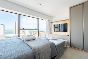 A modern hotel room with a large bed, a TV, and a city view. - Icon Housi in Boa Viagem New 300m From the Sea By Carpediem (Recife)