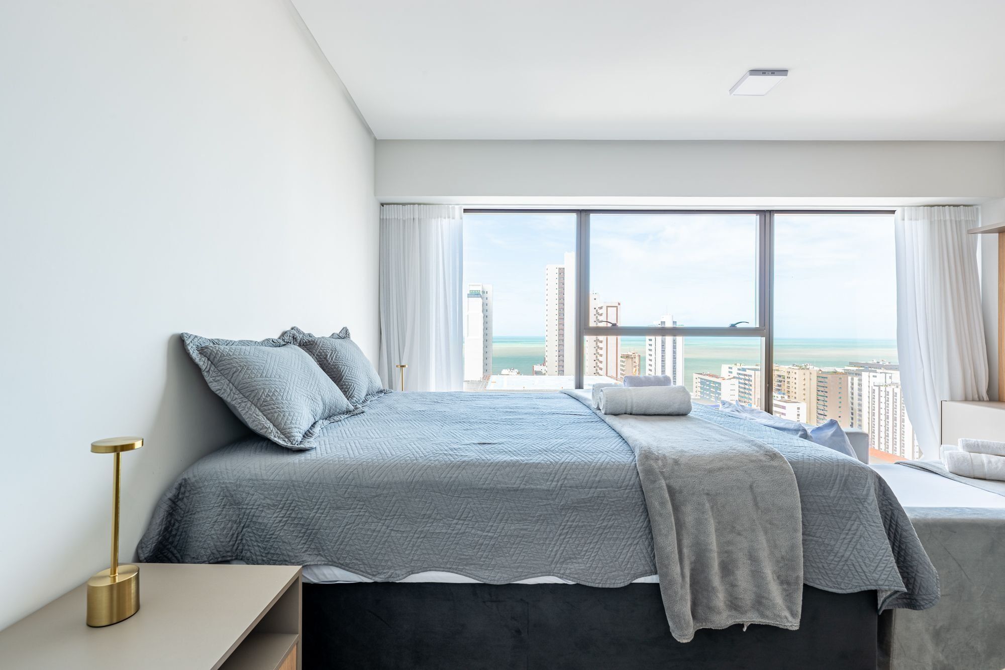 Un dormitorio moderno con una cama grande, una mesita de noche y vistas a la ciudad y al océano.
