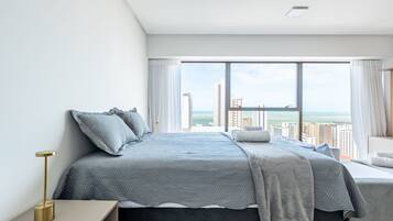 Un dormitorio moderno con una cama grande, una mesita de noche y vistas a la ciudad y al océano.