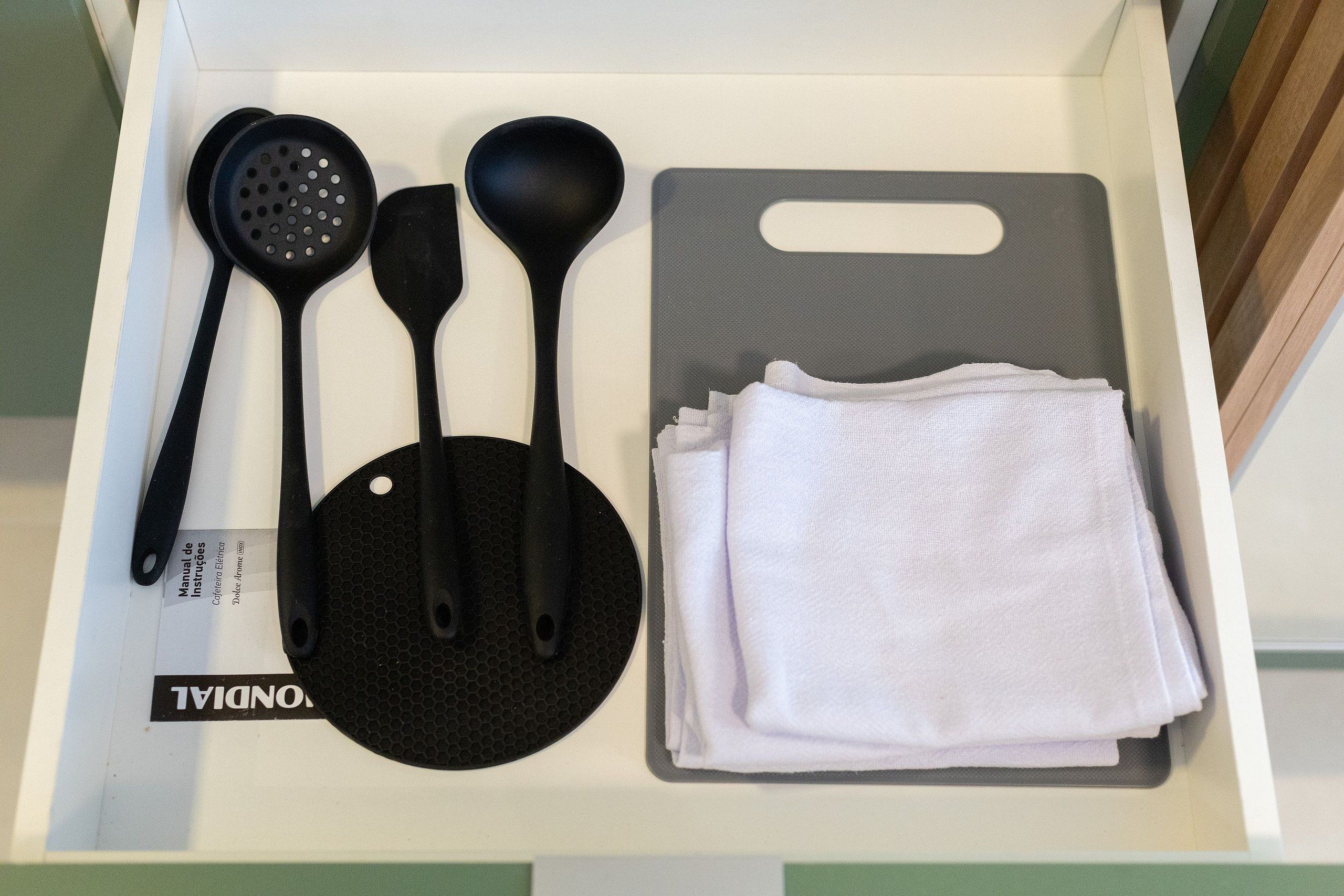 Un cajón con utensilios de cocina negros, una tabla de cortar y una pila de servilletas de tela blancas.