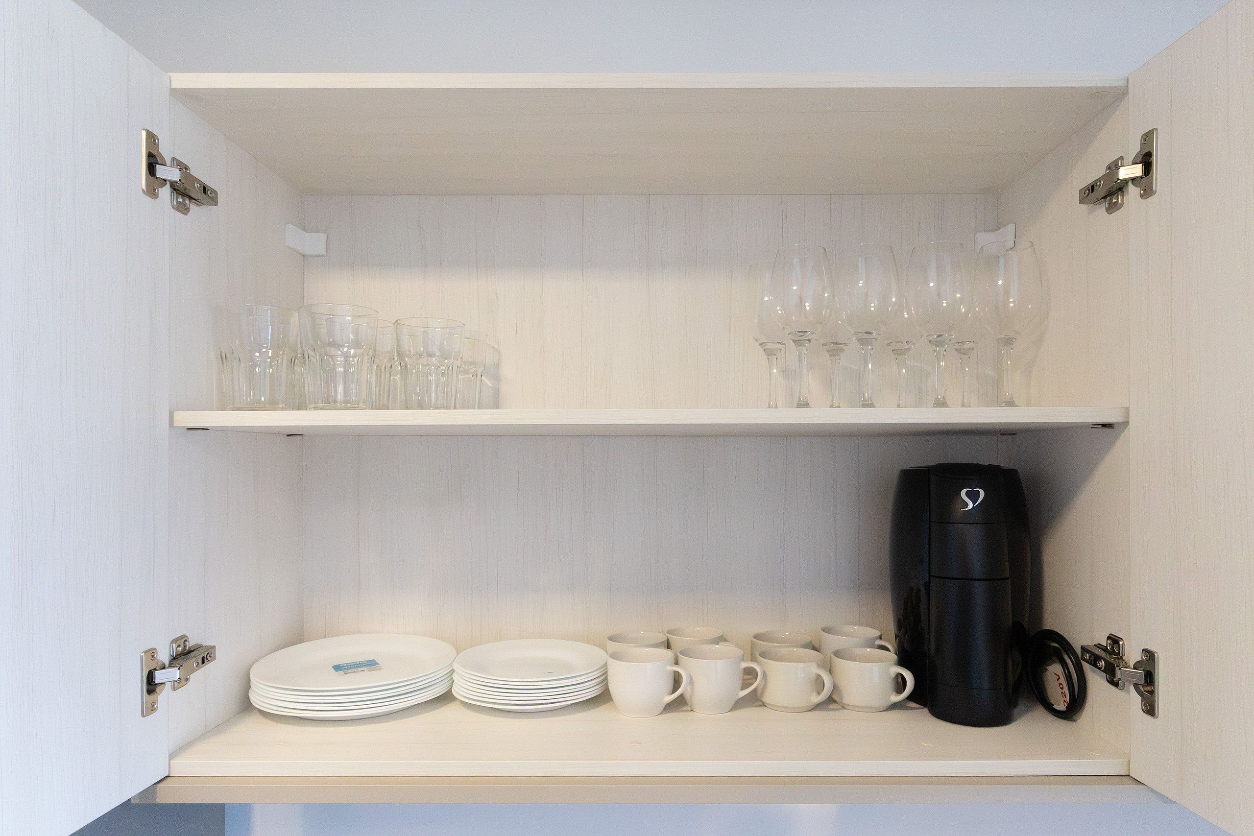 A kitchen cabinet with shelves holding plates, cups, and a coffee maker.