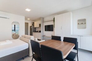 Une chambre d’hôtel moderne comprenant un lit, une table à manger avec des chaises, un coin cuisine et un grand miroir.