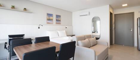 A modern hotel room with a dining area, a sofa, a bed, and a small balcony.