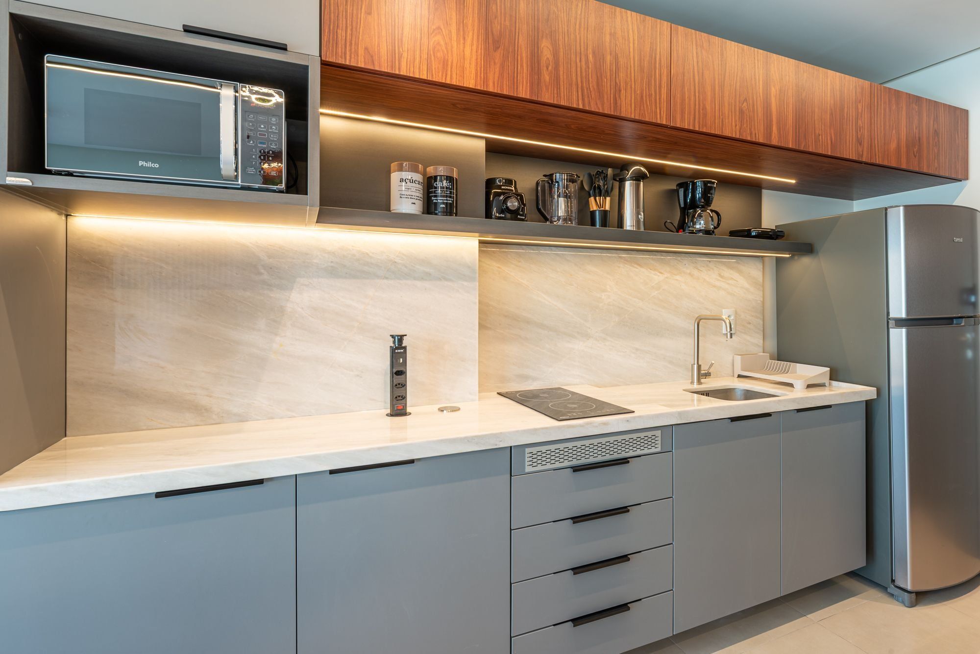 Una cocina moderna con microondas integrado, refrigerador de acero inoxidable y encimera con pileta y cajones de almacenamiento.