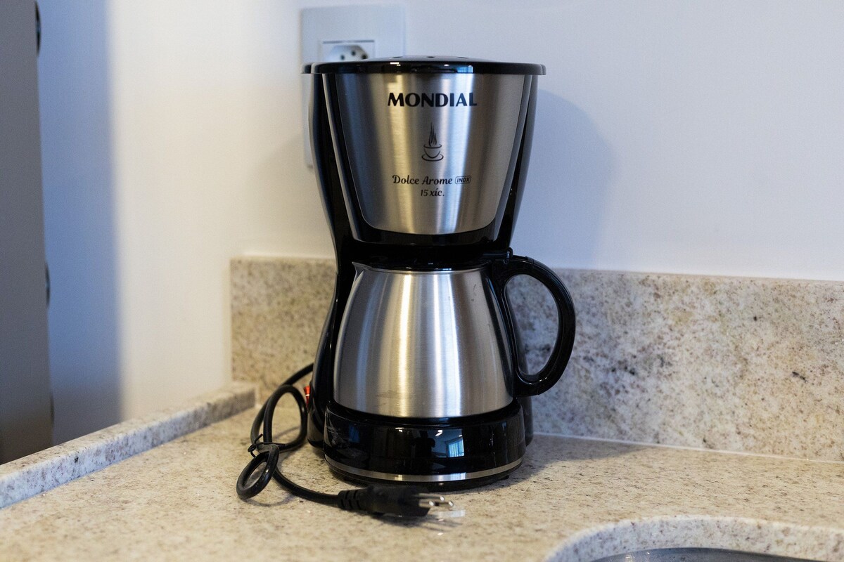 Een koffiezetapparaat van roestvrij staal met een zwarte basis en hendel, met daarop het label 'MONDIAL', op een aanrecht.