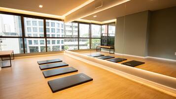 Un gimnasio moderno con suelo de madera, colchonetas de ejercicio y amplias ventanas con vistas a la ciudad.