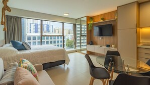A modern hotel room with a large bed, a sofa, a glass dining table, and a TV. - Icon Housi in Boa Viagem New 300m From the Sea By Carpediem (Recife)