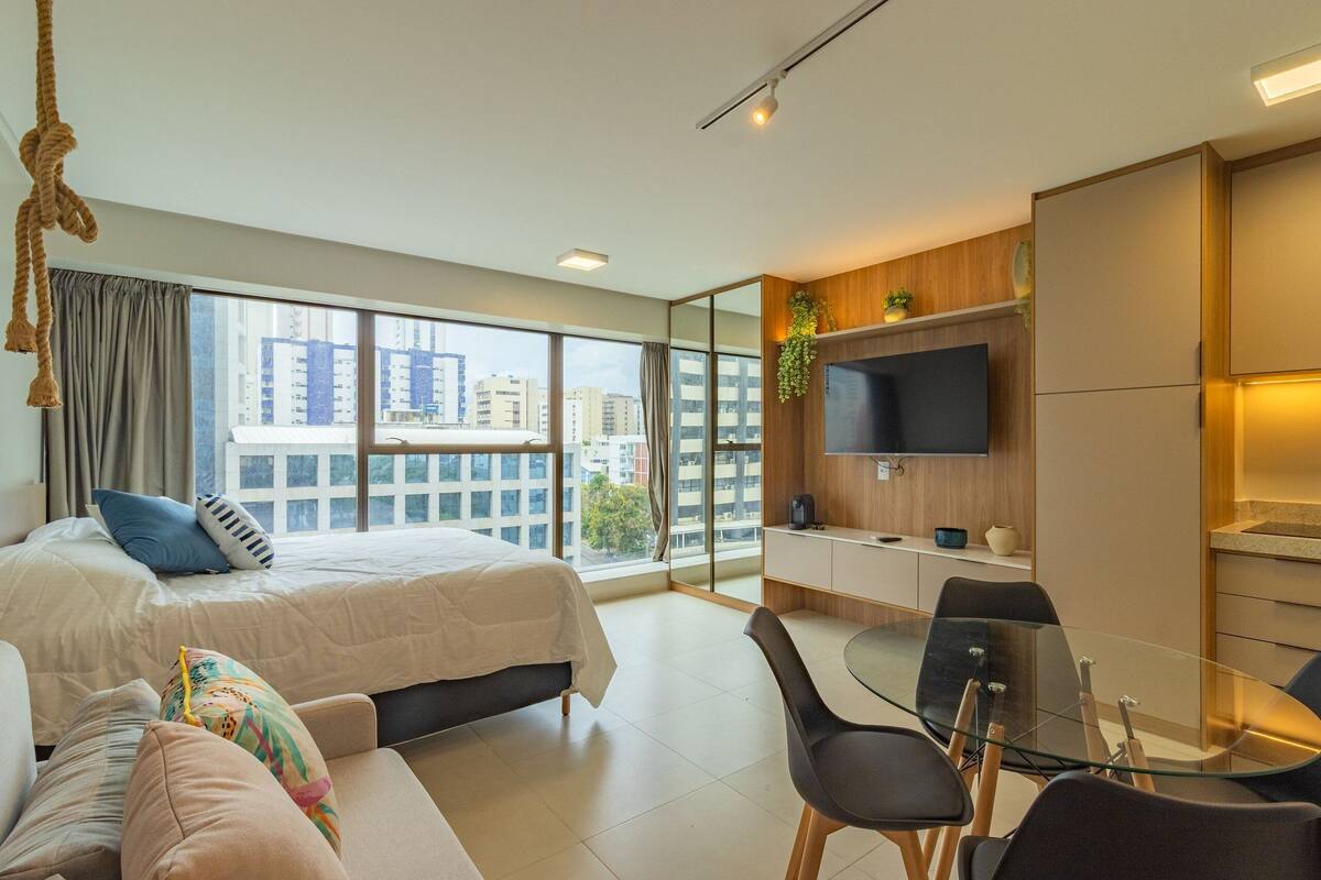 A modern hotel room with a large bed, a sofa, a glass dining table, and a TV.