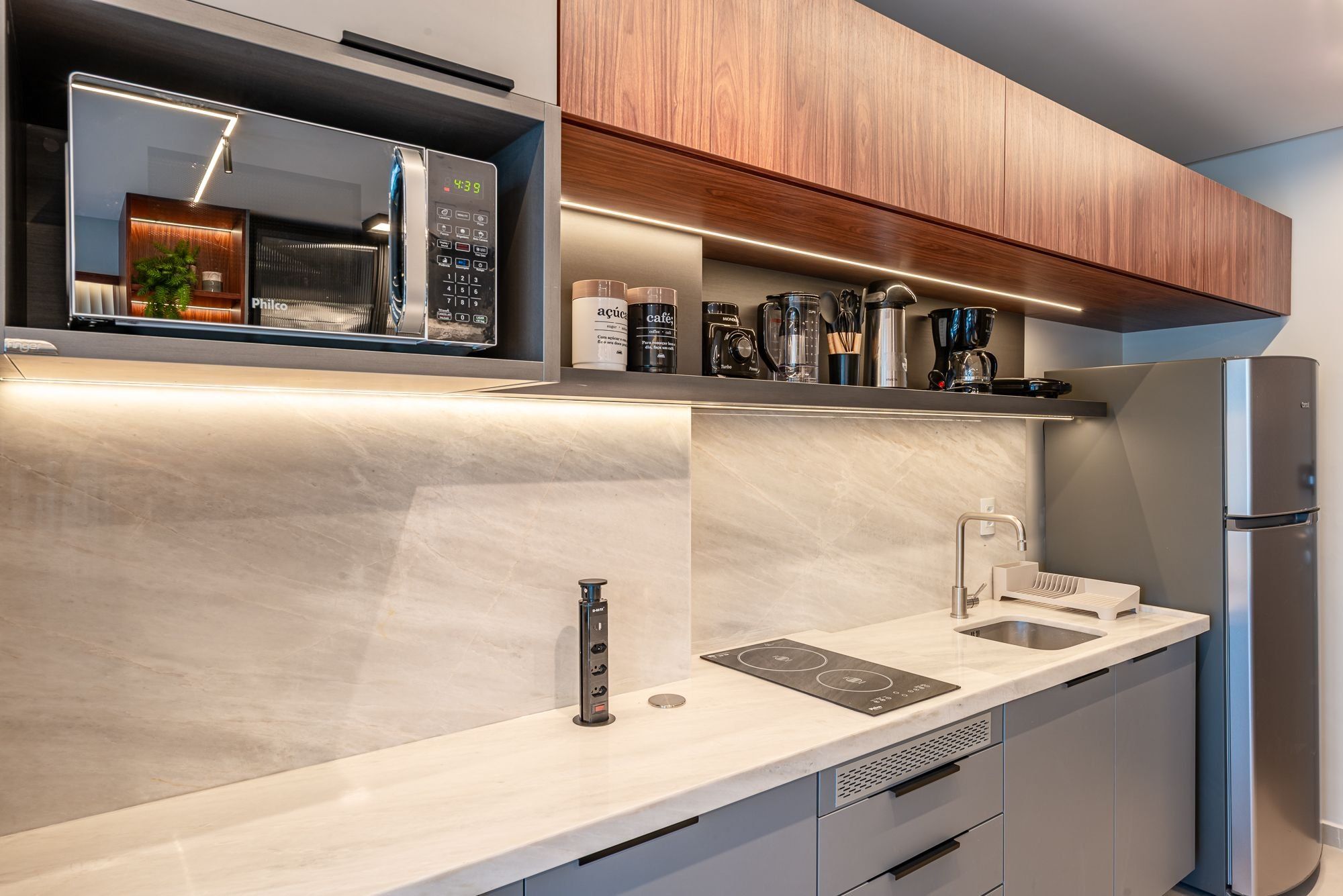 Uma cozinha moderna com micro-ondas integrado, máquina de café e frigorífico.