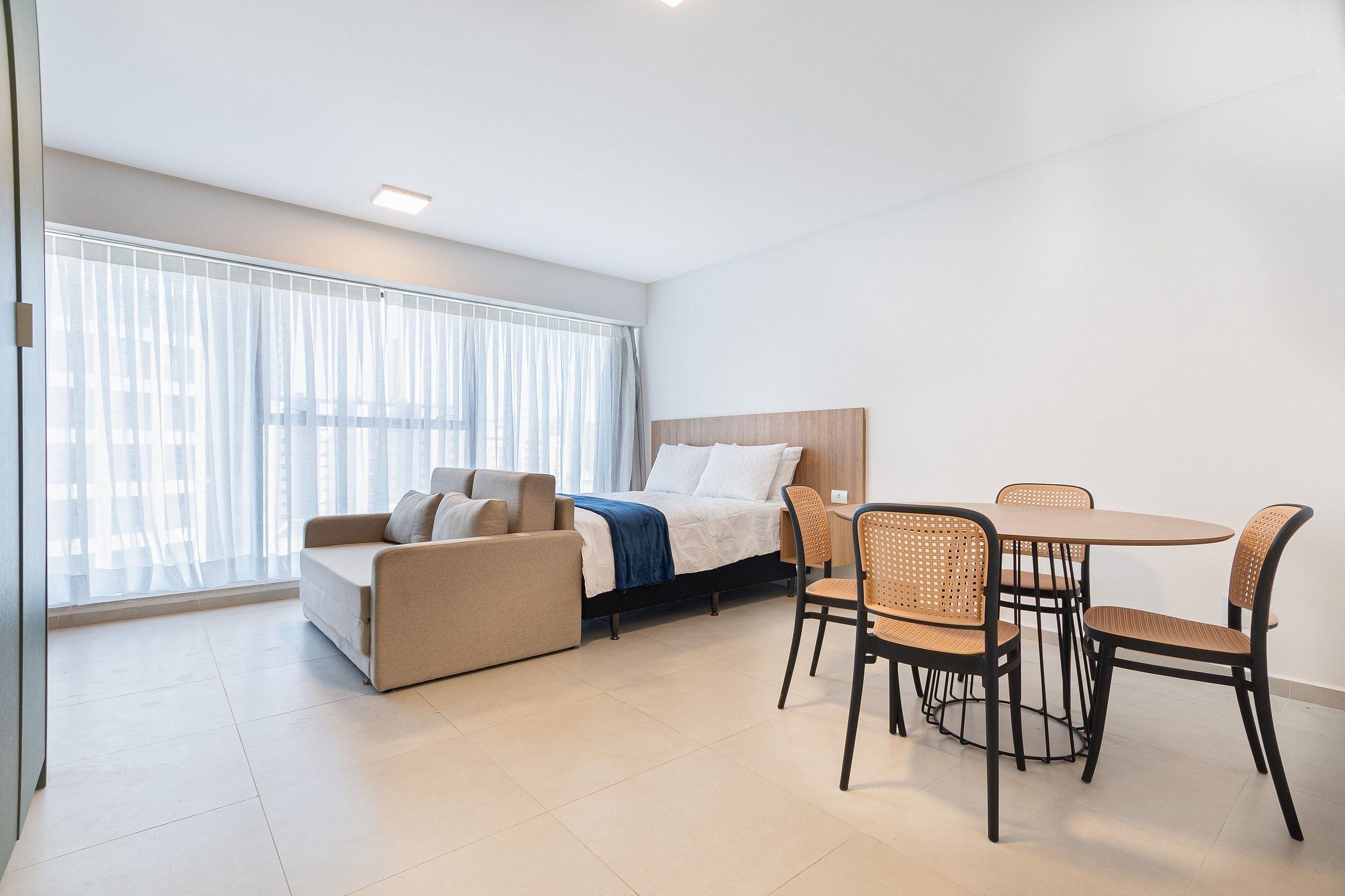 Quarto de hotel moderno com cama, sofá e mesa de jantar com cadeiras.