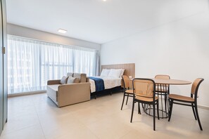 A modern hotel room with a bed, a sofa, and a dining table with chairs. - Icon Housi in Boa Viagem New 300m From the Sea By Carpediem (Recife)